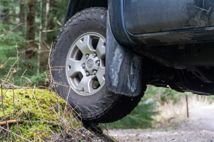 A Nitto Terra Grappler G3 tire flexes on a small rock beside a forest road