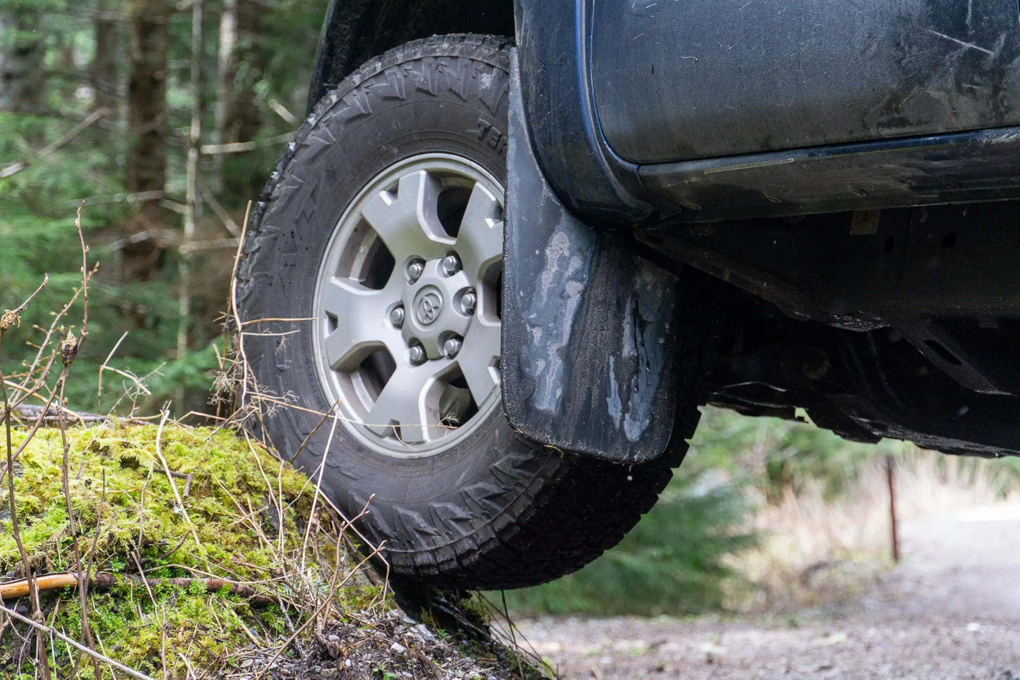 A Nitto Terra Grappler G3 tire flexes on a small rock beside a forest road