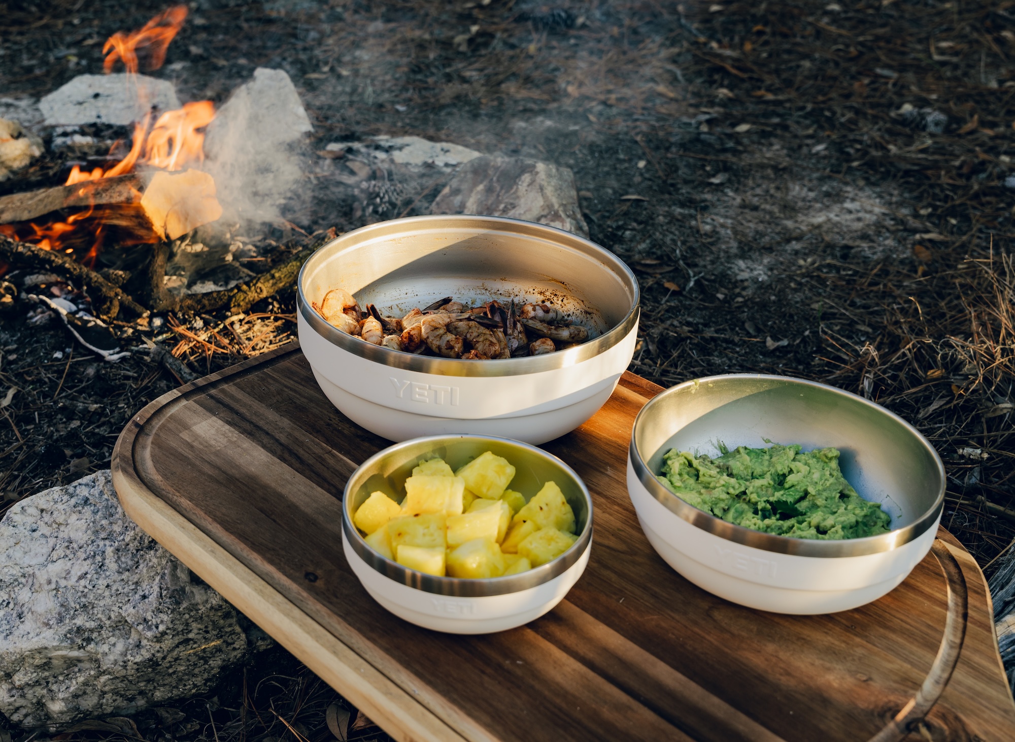 Yeti bowls on wood cutting board next to campfire