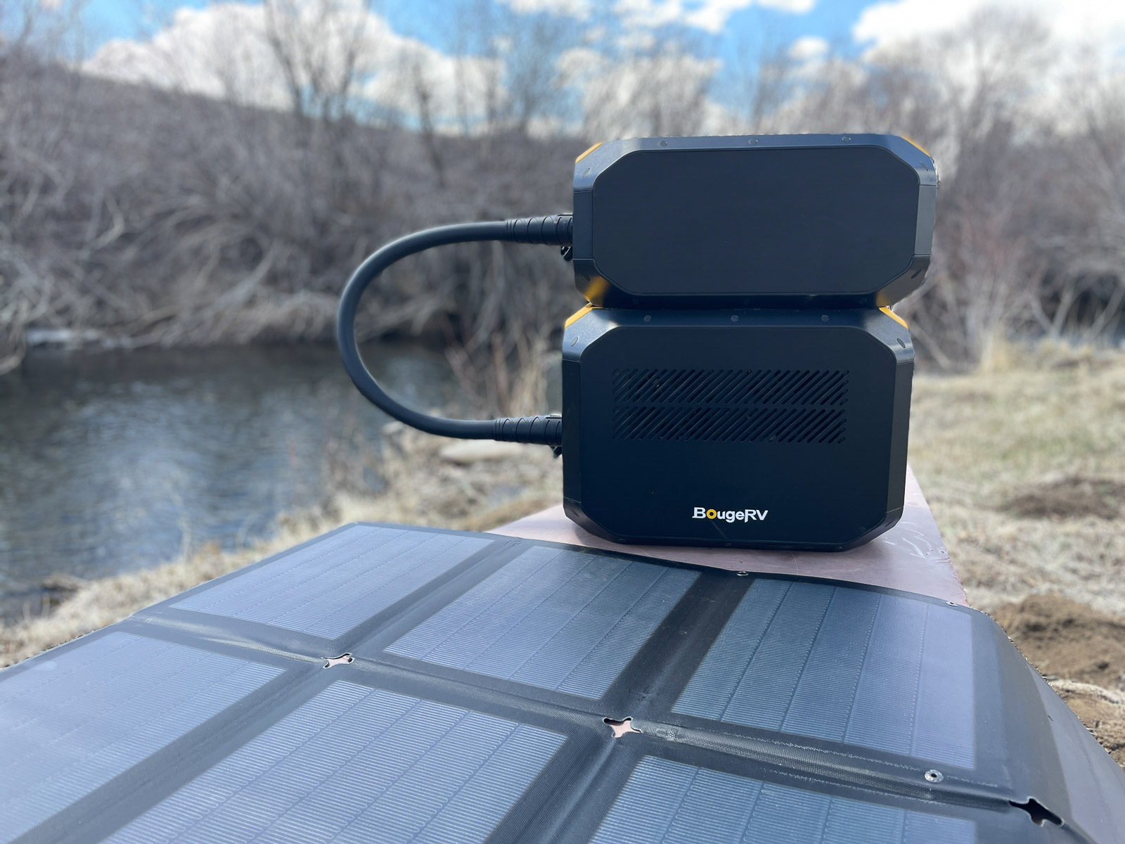 Two expandable battery packs for the Rover2000 power station sit on a table beside a creek