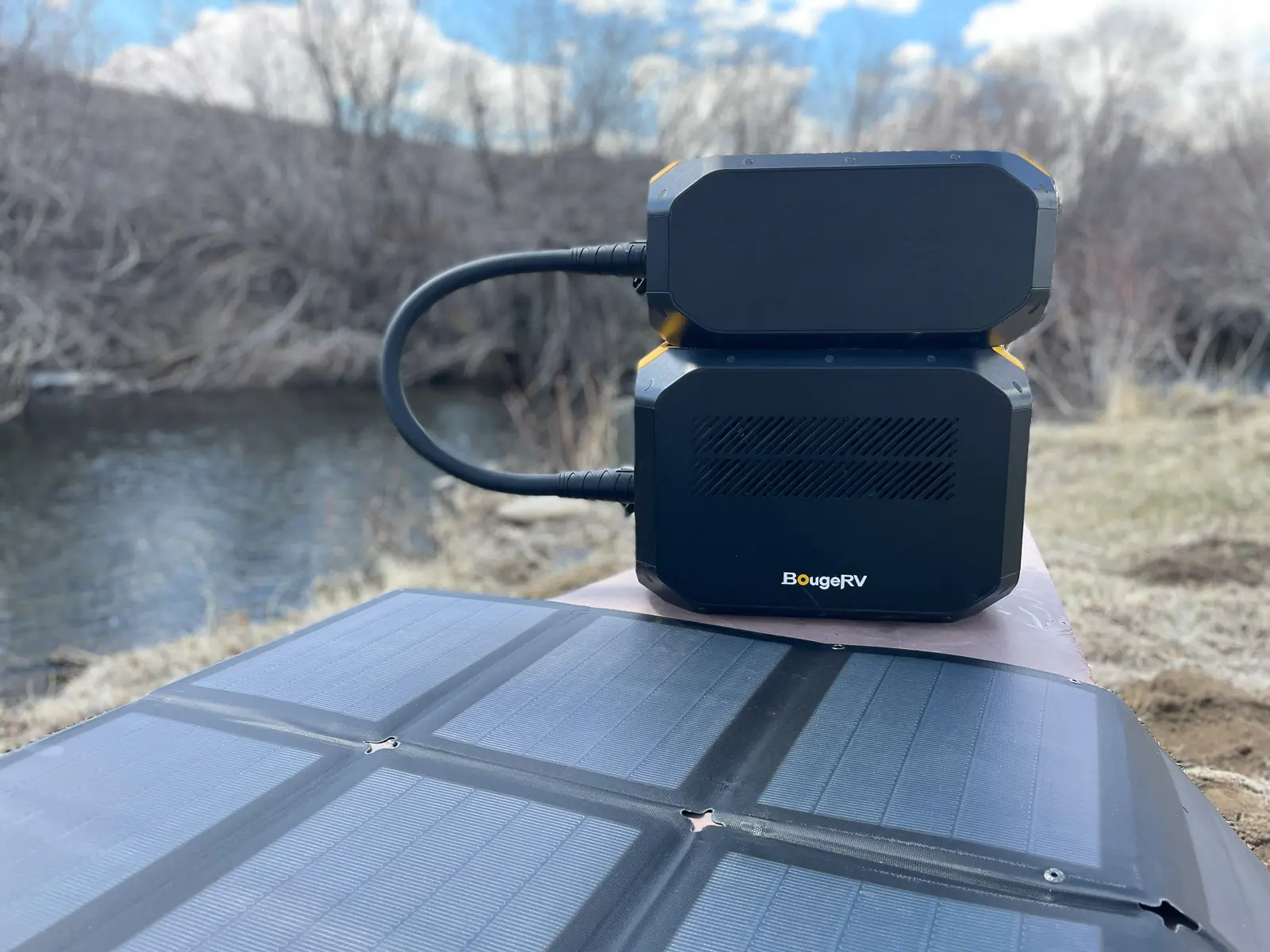 Two expandable battery packs for the Rover2000 power station sit on a table beside a creek