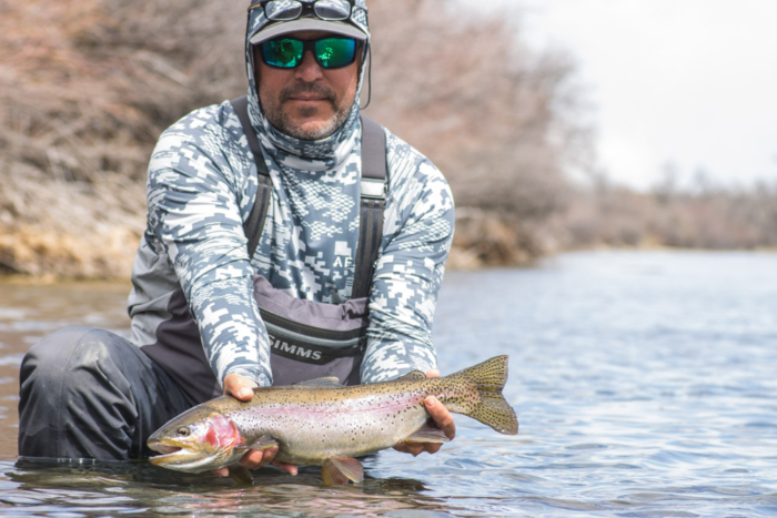 An angler holds a trout while wearing the Simms Flyweight Wader