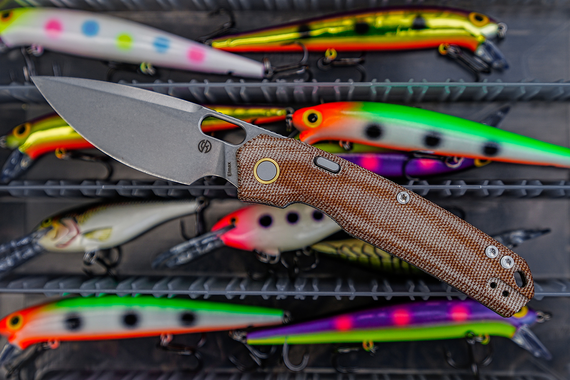 Vosteed Psyop Micarta knife resting on a colorful tackle box with lures