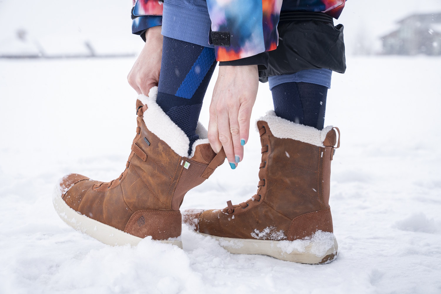 Person adjusting brown Stio Colter boots in the snow.