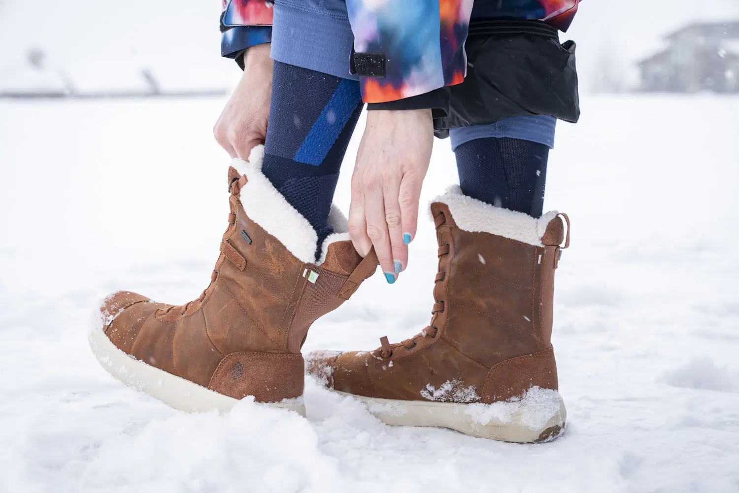 Person adjusting brown Stio Colter boots in the snow.