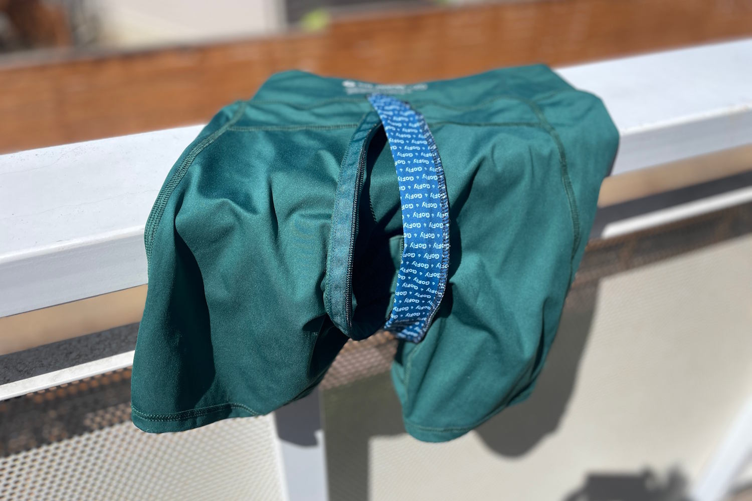 Gnara Go Free green shorts with blue inner panel, draped on a balcony railing