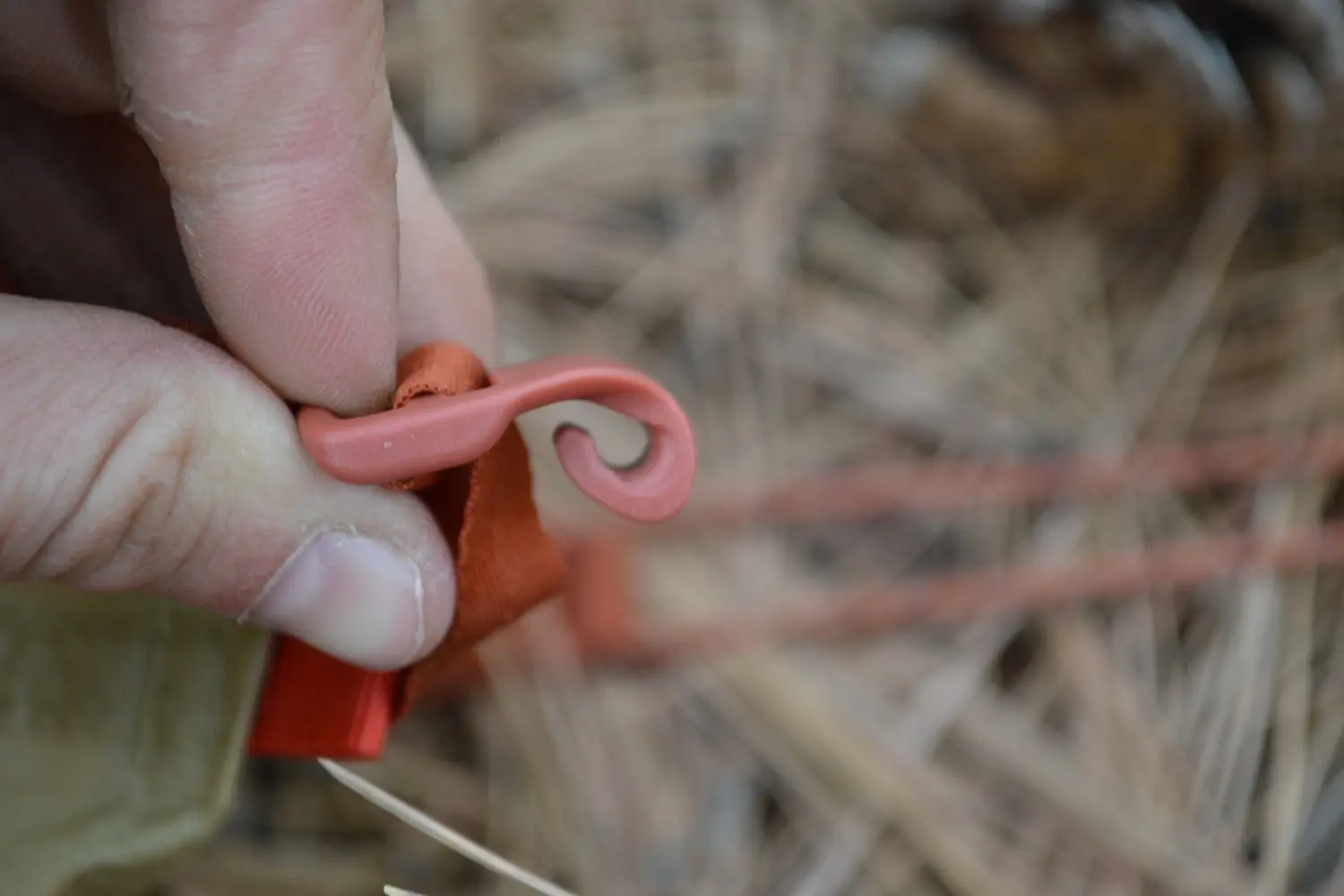 A close-up of a person’s fingers holding a small red silicone hook attached to an orange fabric loop