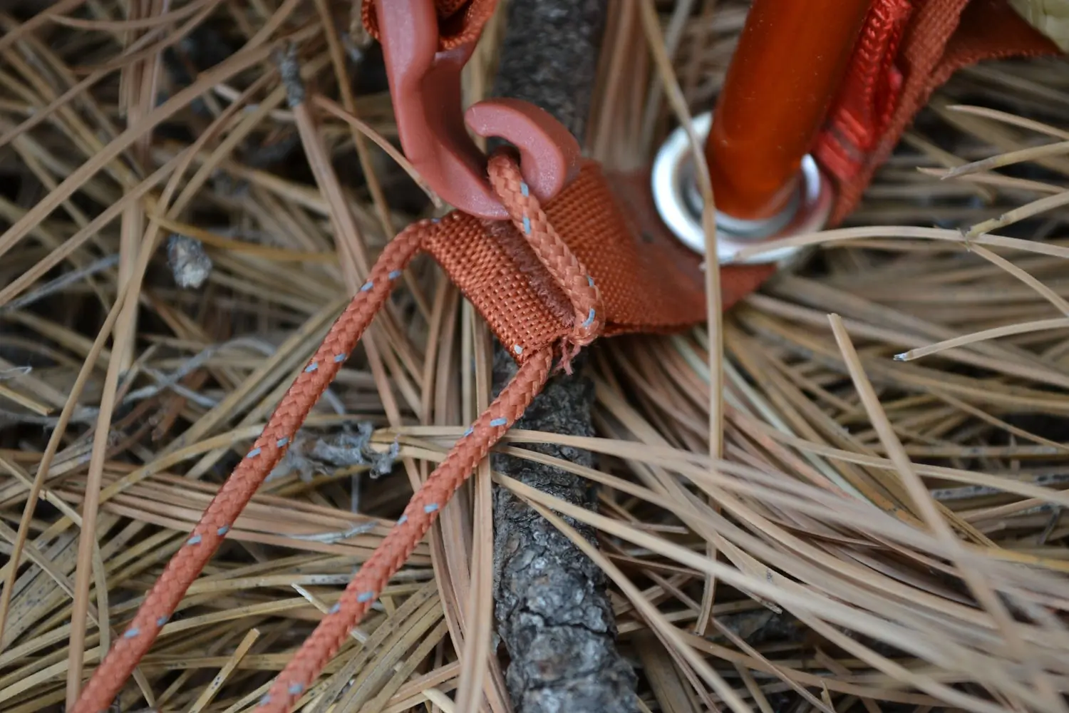 Close-up of a tent rainfly attachment mechanism featuring an orange strap with a plastic hook.