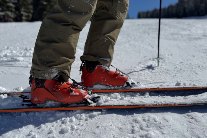 A close-up of a skier's feet wearing bright orange Tecnica ski boots