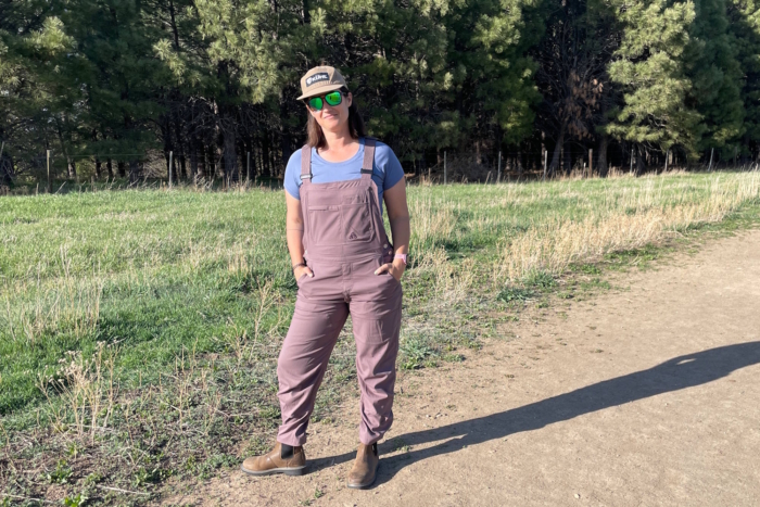 Woman wearing Ecotrek Overalls paired with a blue t-shirt, standing with hands in pockets