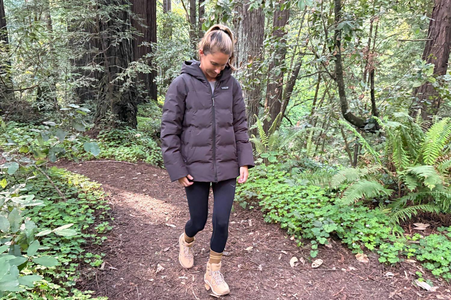 Woman walking on a forest trail in a puffer jacket and hiking boots