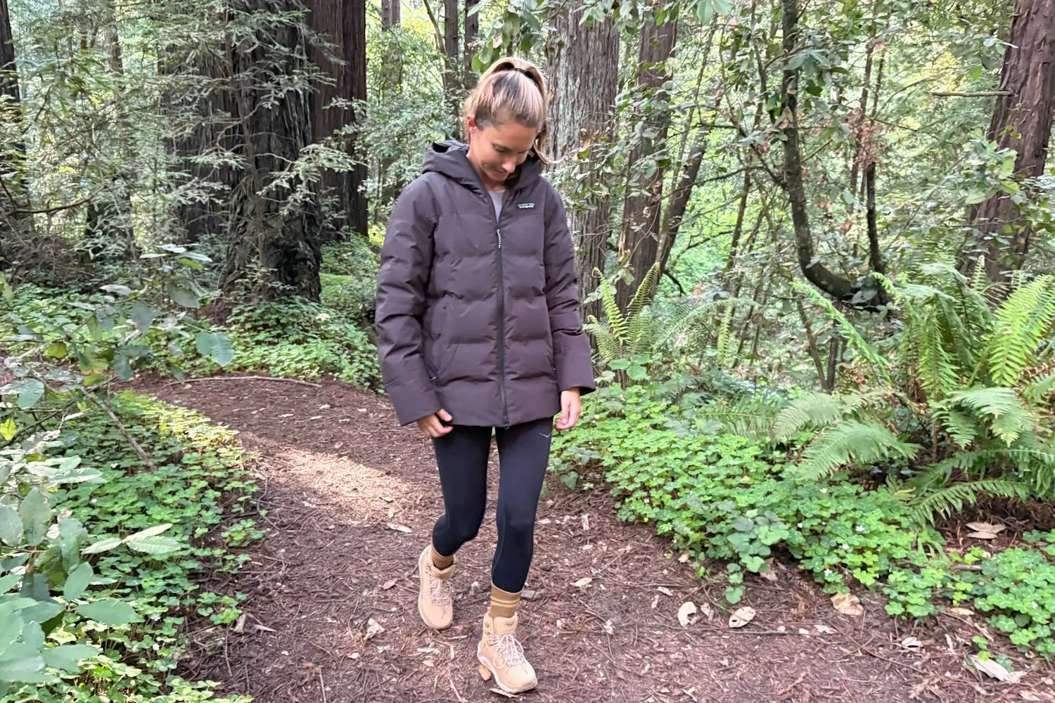 Woman walking on a forest trail in a puffer jacket and hiking boots