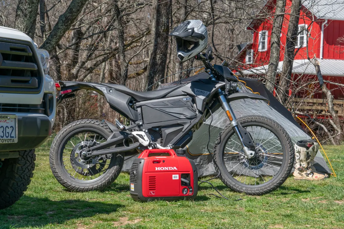The Zero FX electric motorcycle parked next to a Honda generator, tent, and off-road gear in a camping setting