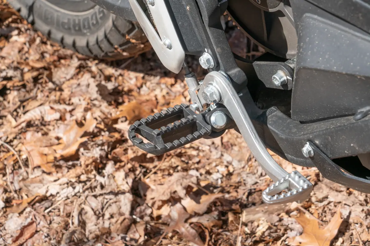 A close-up of the Zero FX electric motorcycle's footpeg and gear lever, with a textured surface and sturdy construction