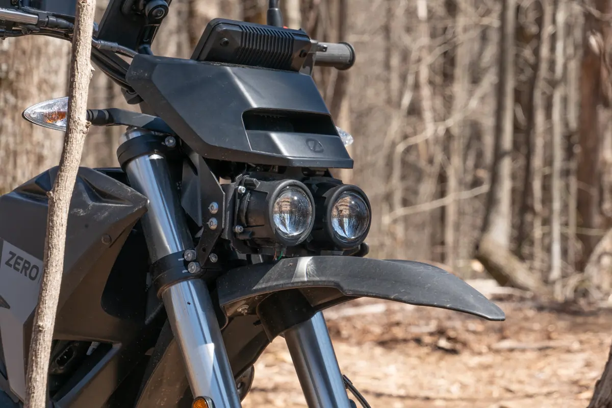 The front view of the Zero FX electric motorcycle, showing the dual headlights and fork suspension, with a wooded background