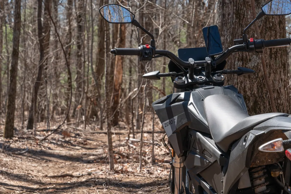 The handlebars of the Zero FX electric motorcycle with a smartphone mount, set against a wooded trail background