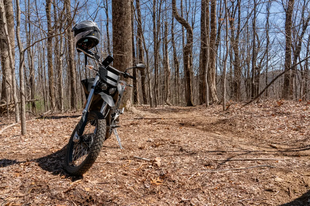 The Zero FX electric motorcycle parked in the forest with a helmet resting on the handlebars, surrounded by trees