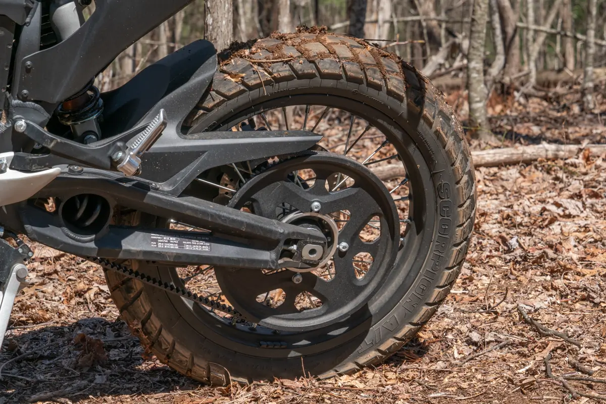The rear wheel of the Zero FX electric motorcycle, featuring the Scorpion tire and drive system in a forest setting