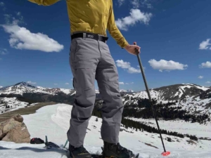 A person wearing Stio Environ pants and red ski boots, standing on skis in the snow