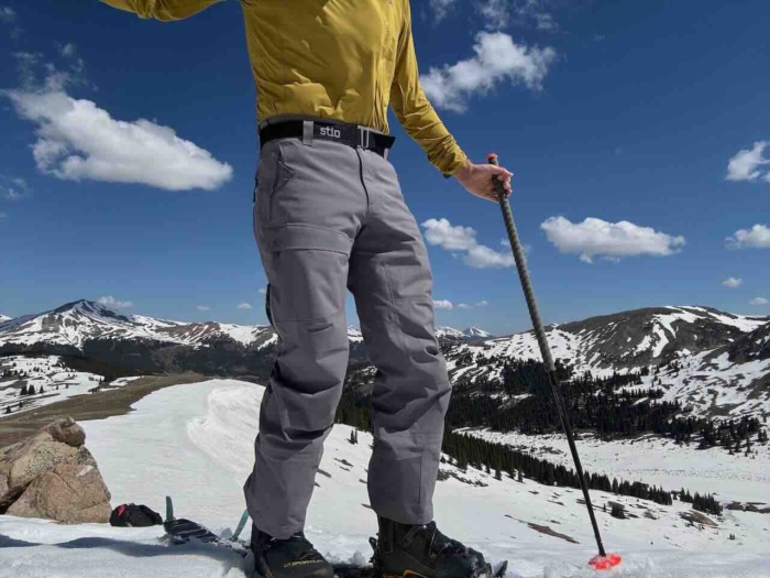 A person wearing Stio Environ pants and red ski boots, standing on skis in the snow