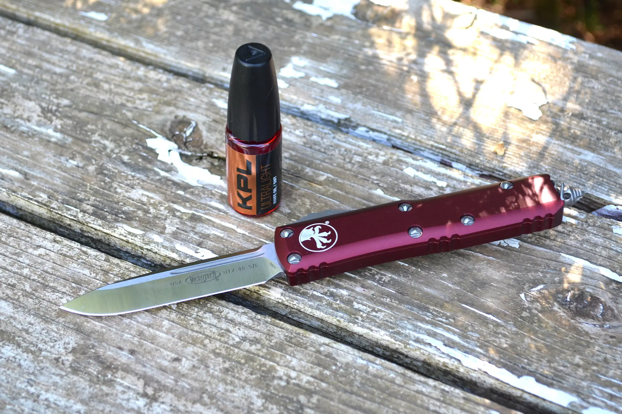 Microtech UTX-85 next to KPL Ultralight oil on a wooden bench
