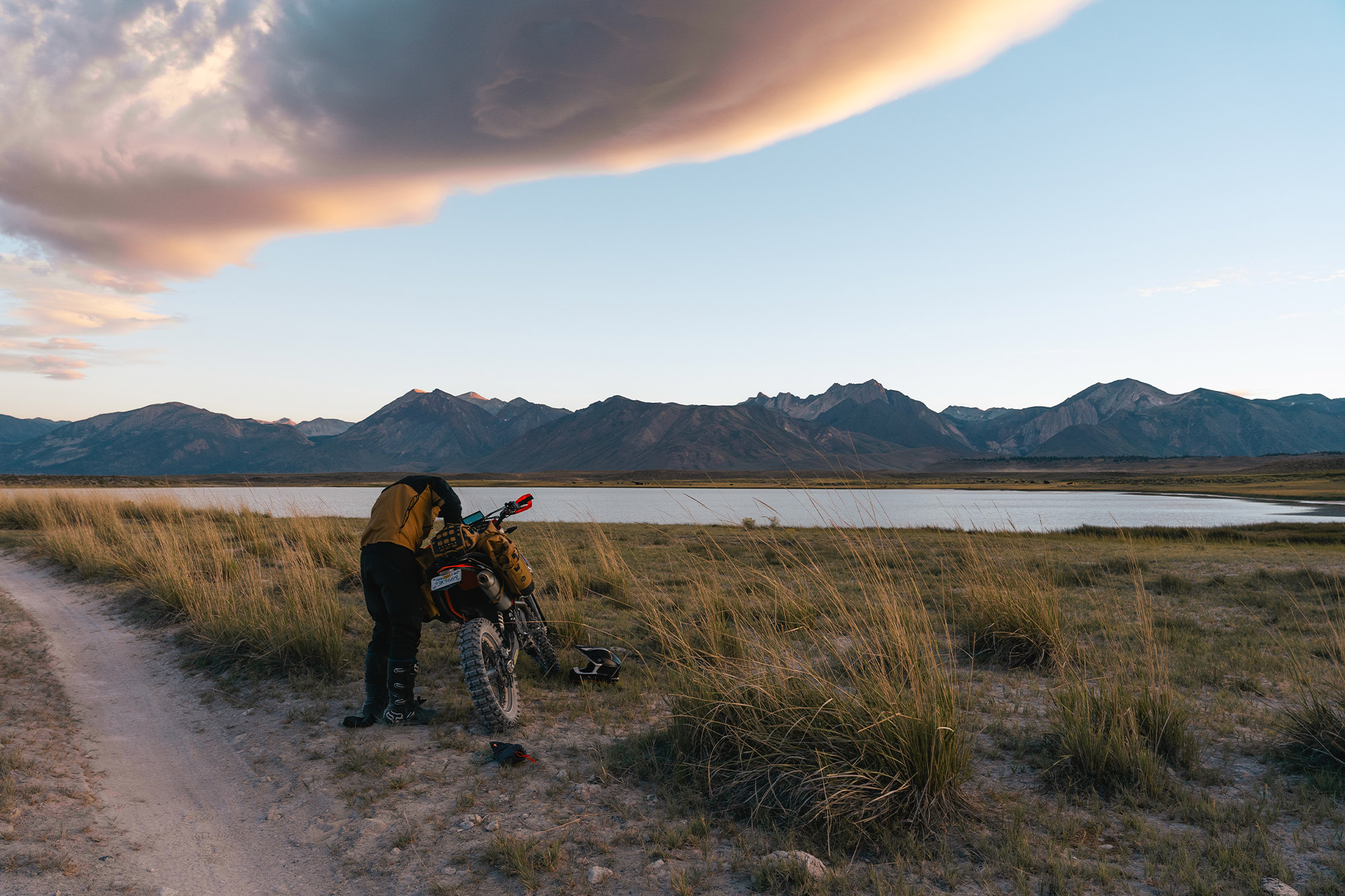 Mosko Moto Reckless 40L System V4.0 beside a rider adjusting gear near a mountain lake