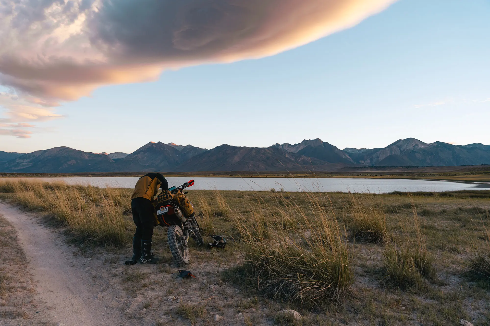 Mosko Moto Reckless 40L System V4.0 beside a rider adjusting gear near a mountain lake