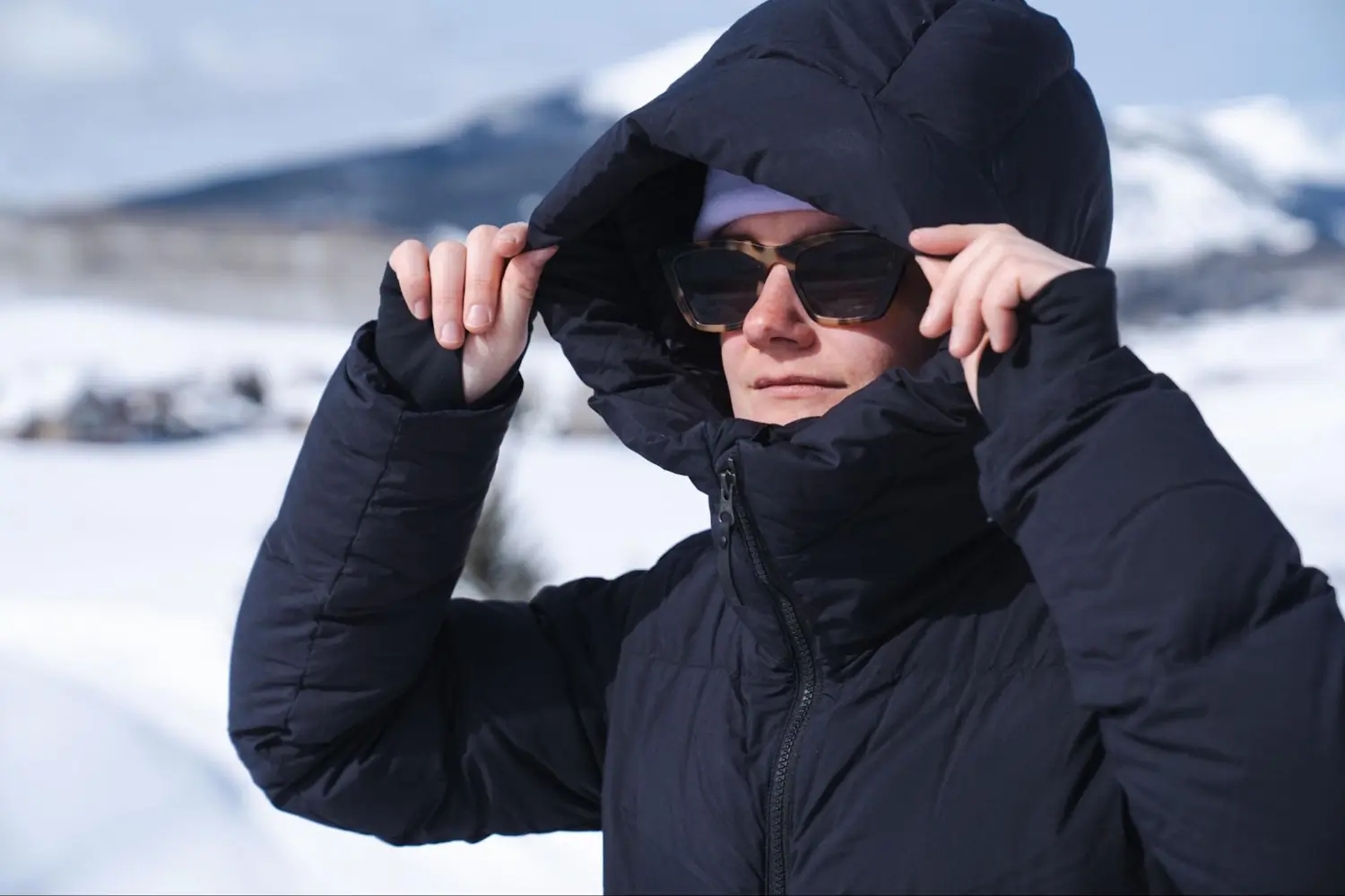 Woman using the insulated hood of the Outdoor Research Coze Down Parka to cover her face for protection in snowy conditions
