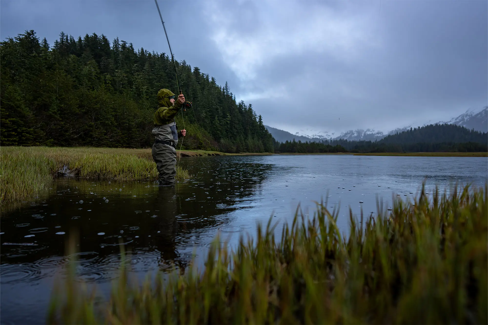 Patagonia Swiftcurrent Traverse Waders standing mid-stream while fly fishing in the rain