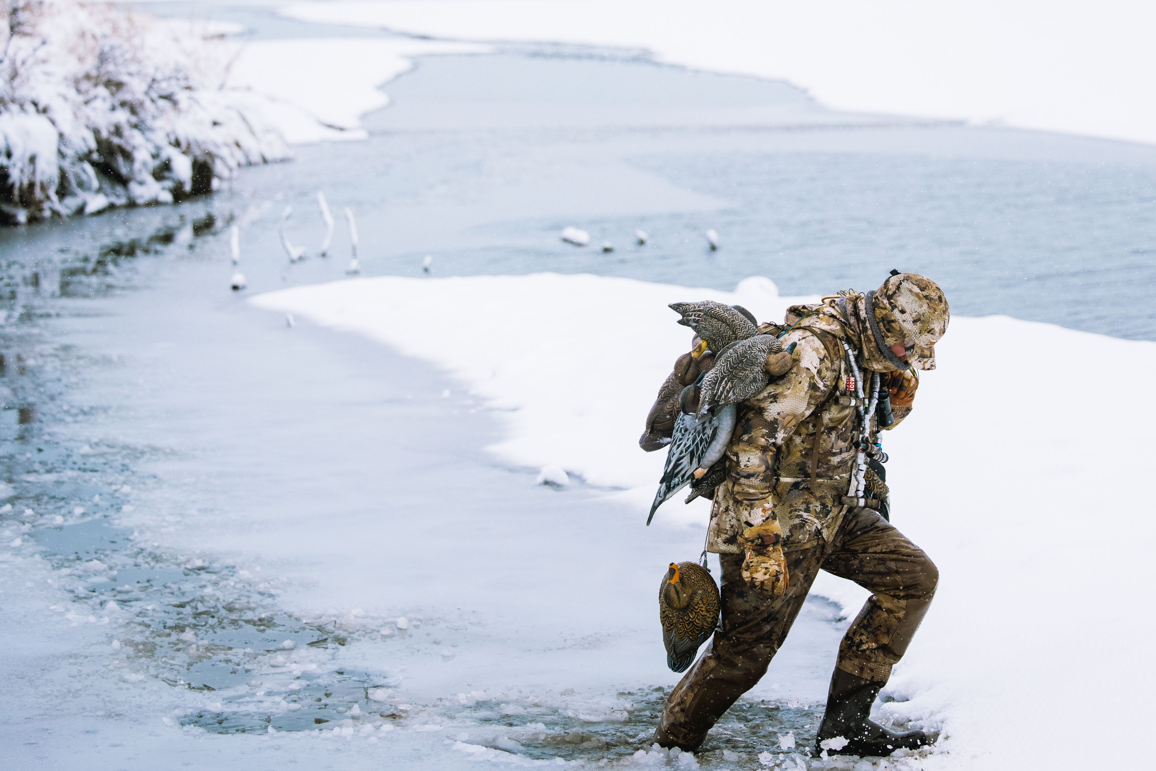 A hunter walking across a frozen stream in the Sitka Delta Pro Waders