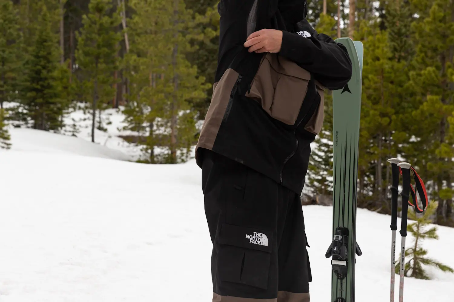 A person adjusts the underarm vent of a The North Face Dragline jacket while standing in a snowy forest