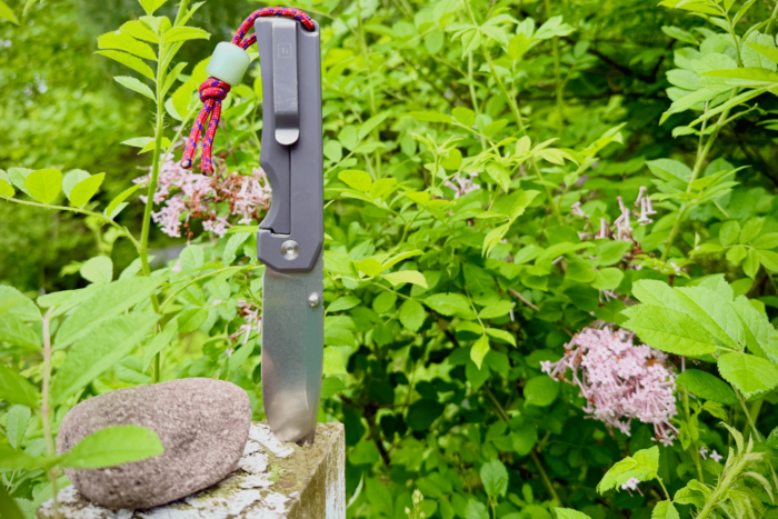 Big Idea Design Ti Pocket Knife II standing upright outdoors with greenery behind