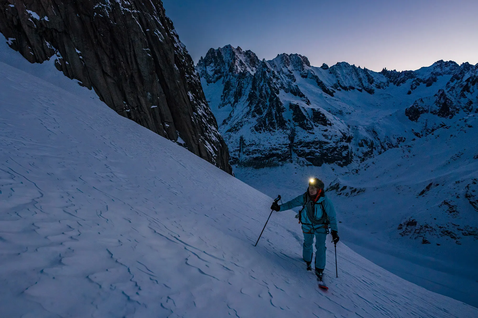 Vivian ascends a snowy slope at dawn with a headlamp