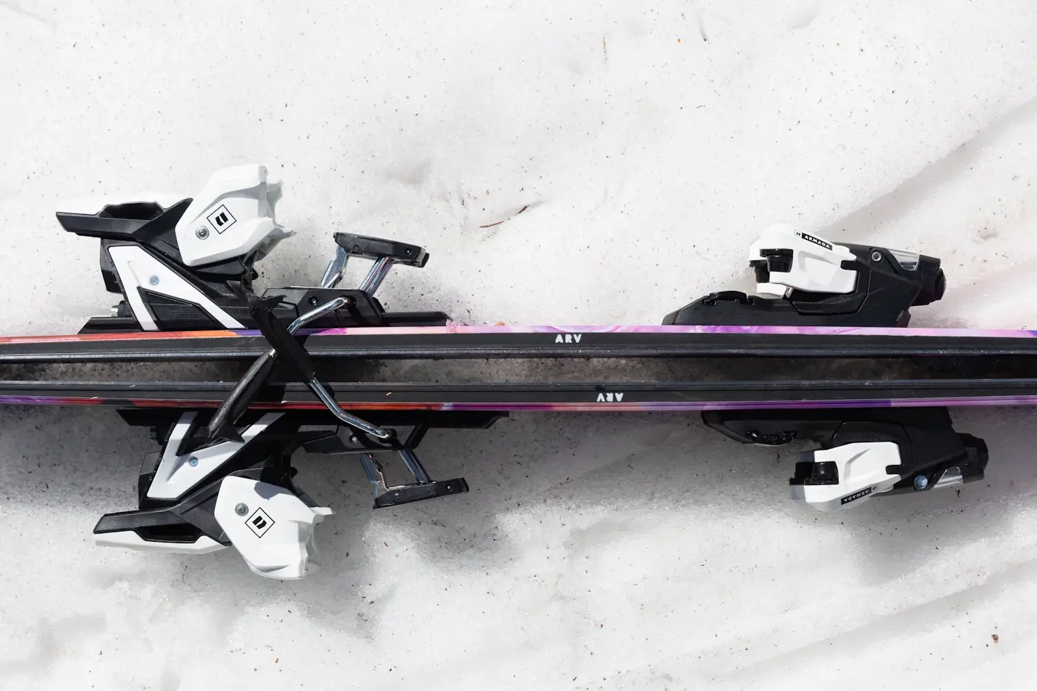Close-up view of two pairs of Armada ARV 100 skis with white and black bindings, resting base-to-base on snow.