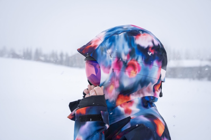 A person in a Burton snow jacket with the hood pulled up, standing in snow
