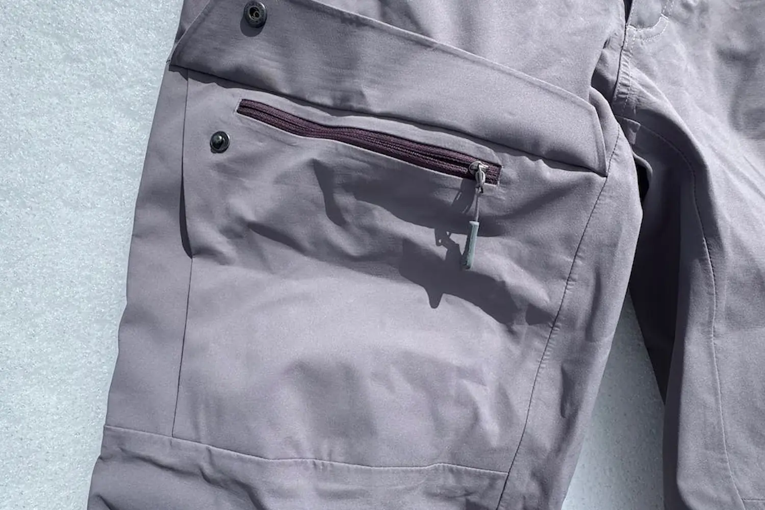 Close-up of a pair of environ pants lying on snow, showing a zippered thigh pocket.