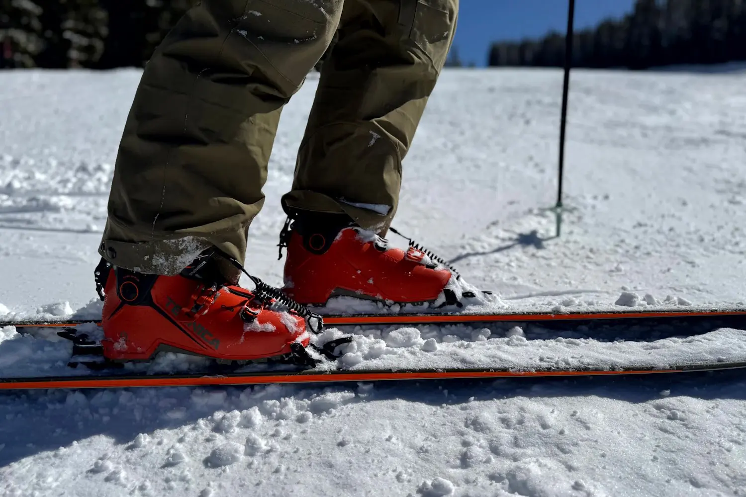 Skier wearing Flylow Chemical Pants and orange ski boots on snow.