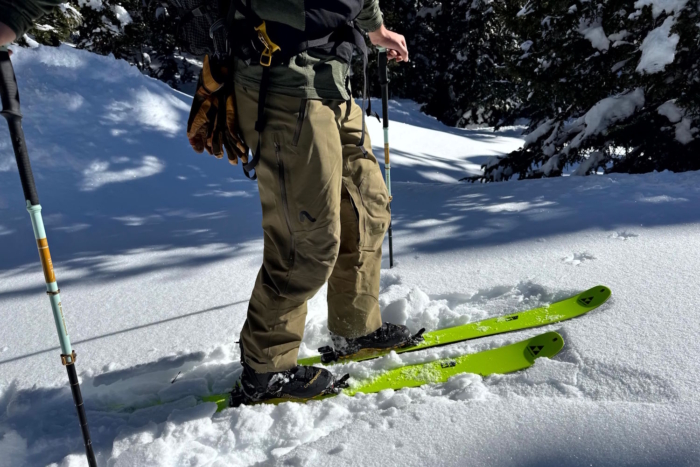 Person on skis in snow, wearing Flylow pants and holding trekking poles.