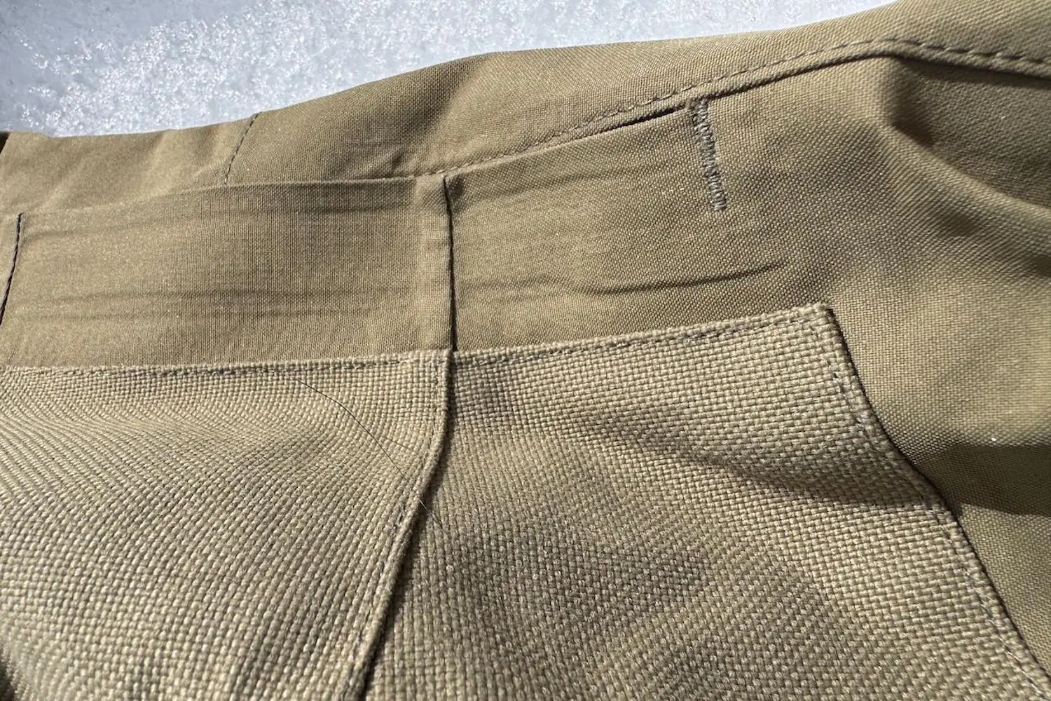 Close-up of tan-colored Flylow Chemical Pants showing the durable textured reinforcement patch at the knee and detailed stitching