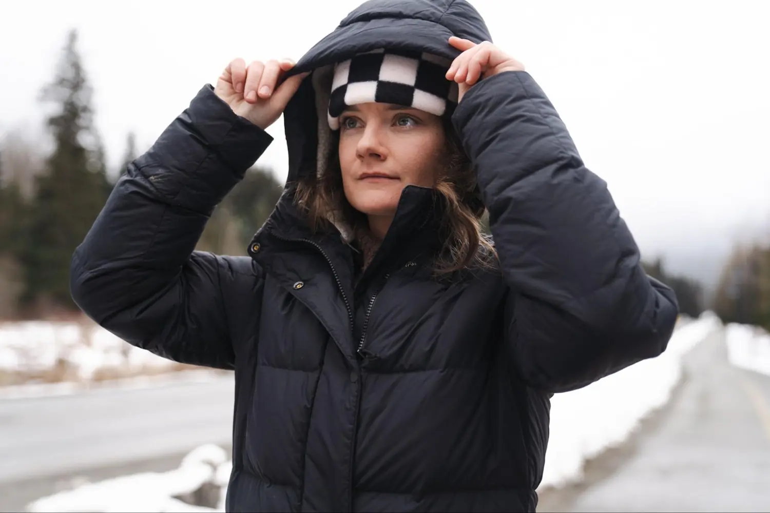 Woman adjusts the hood of her REI Norseland down parka while standing on a snowy roadside