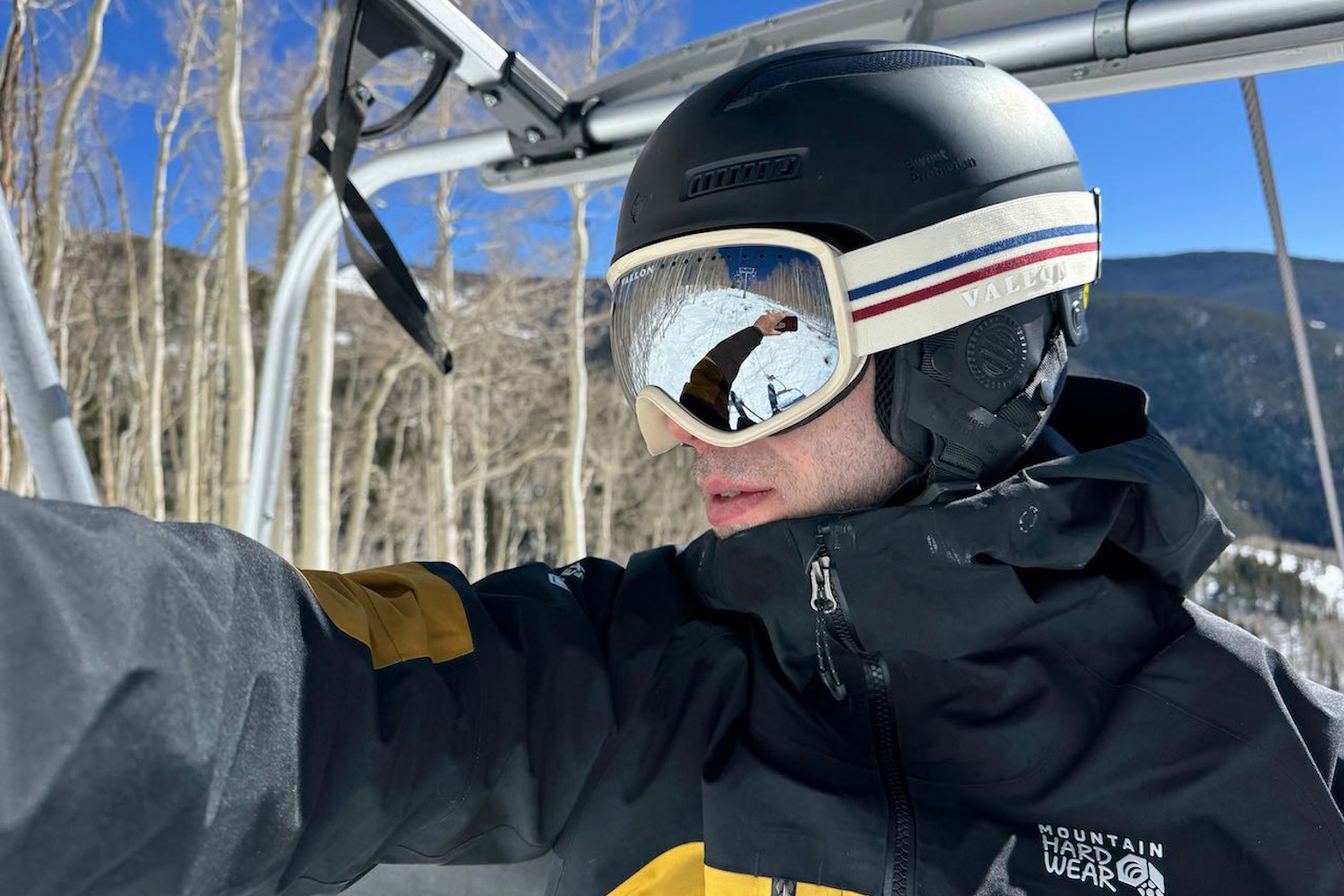 Skier wearing Vallon Freebird goggles and a black helmet, sitting on a ski lift