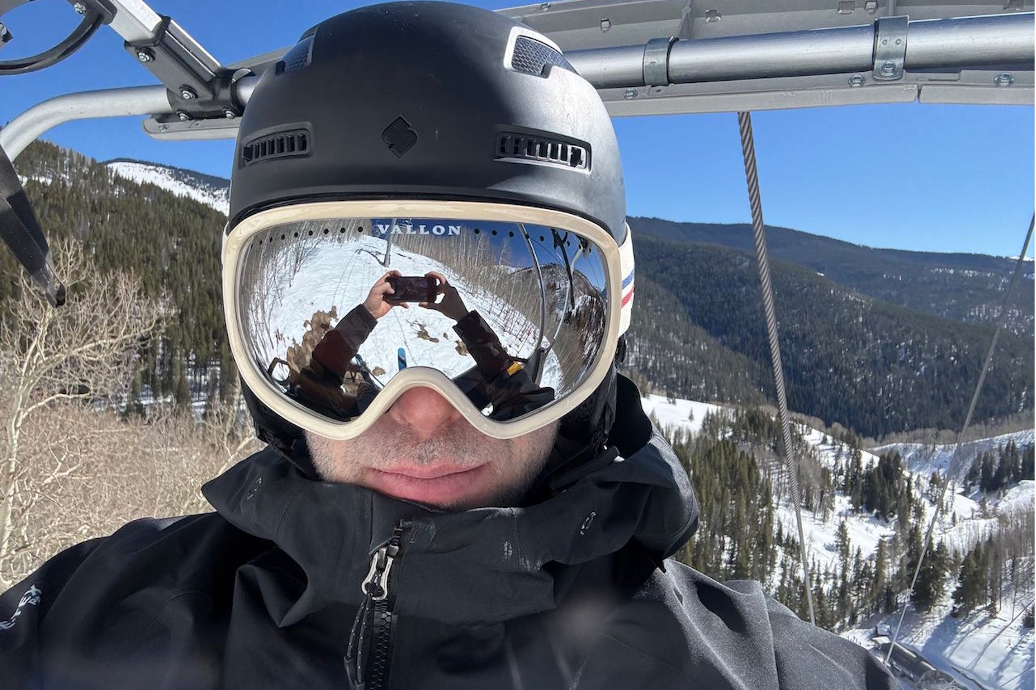 Skier wearing Vallon Freebird goggles and a black helmet, sitting on a ski lift