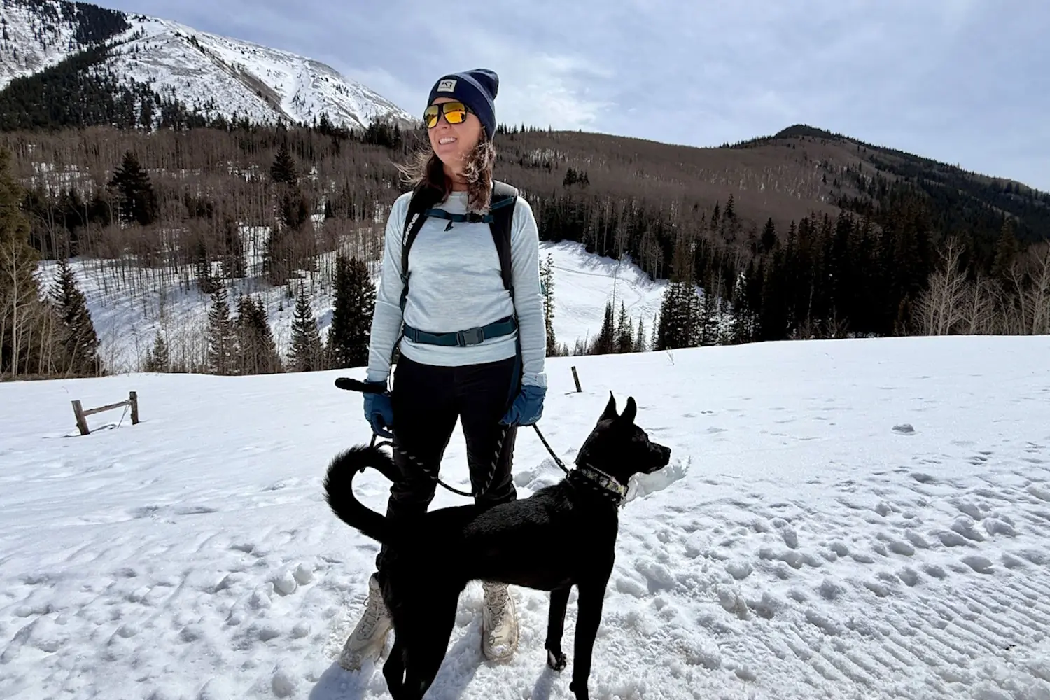 A woman standing in the snow wearing Smartwool base layers, accompanied by her dog.