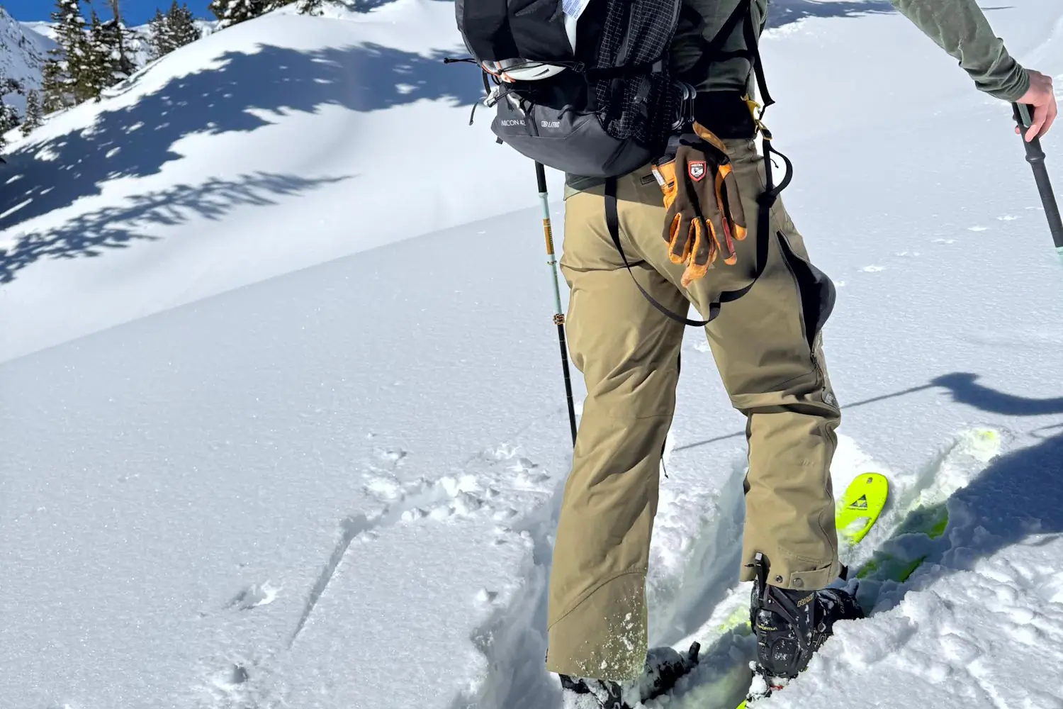 Skier ascending snowy slope wearing Flylow Chemical Pants and carrying a backpack.