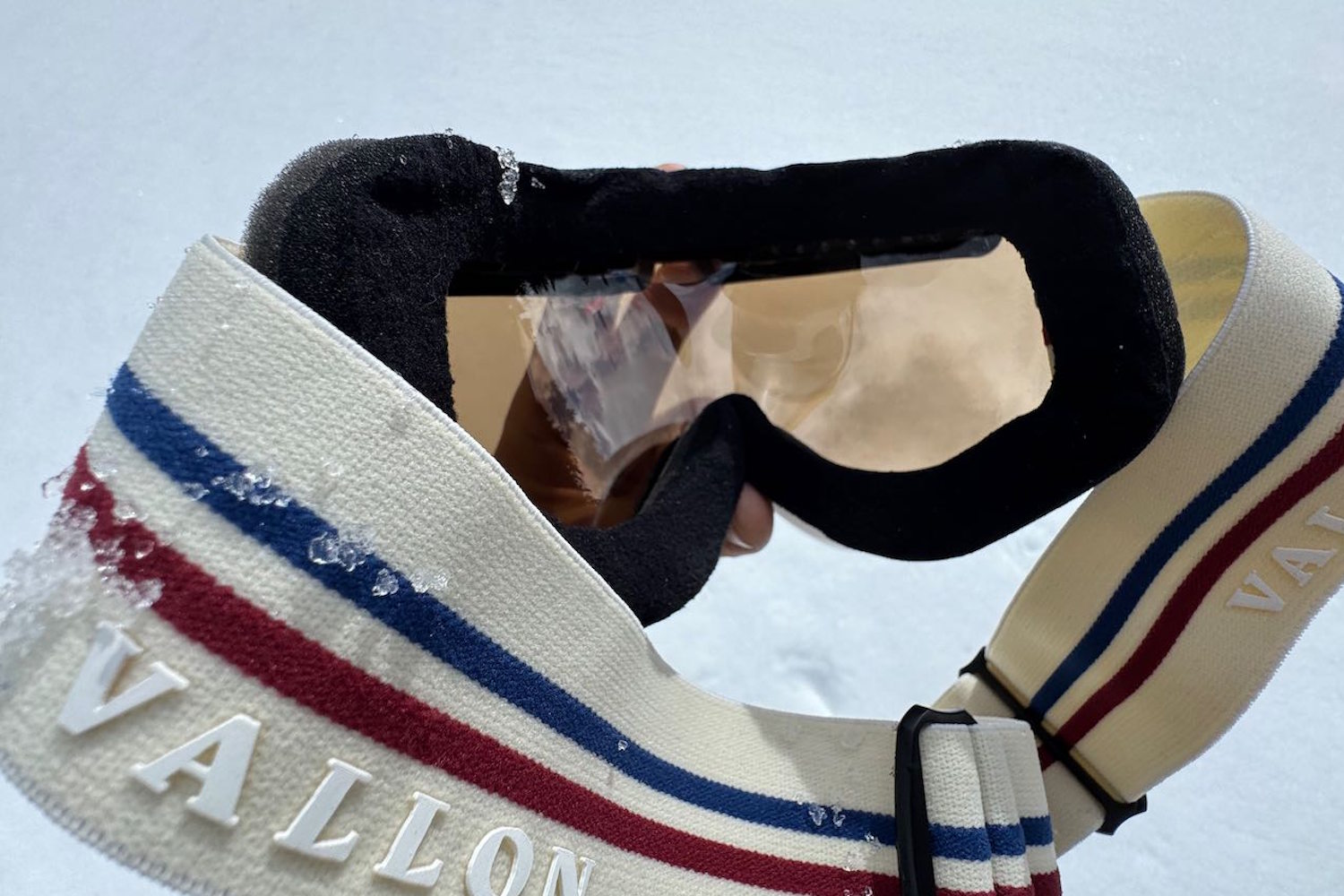Vallon Freebird ski goggles held in hand over snow, showing lens and cream strap