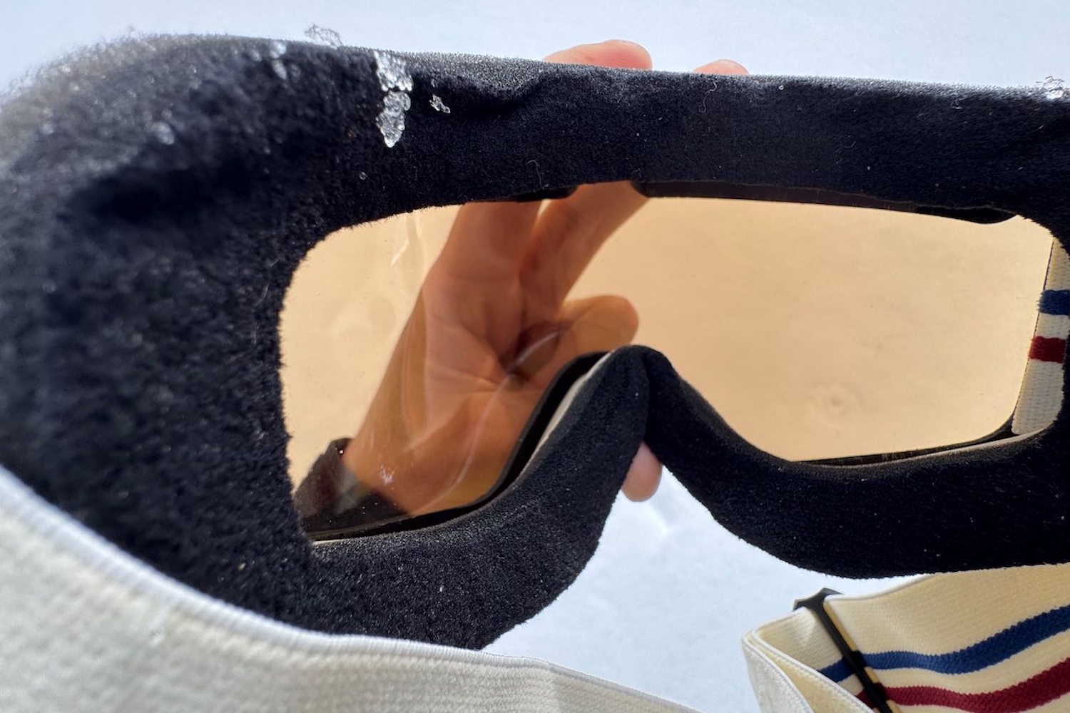 A close-up view of the inside of a pair of Vallon Freebird ski goggles held up against a snowy background.