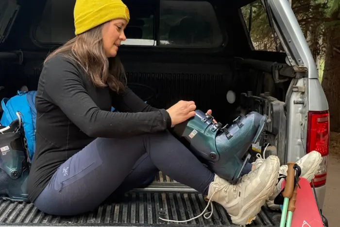 A woman wearing an Arc'teryx Satoro crew neck shirt, matching leggings, and a yellow beanie sits on the tailgate of a truck