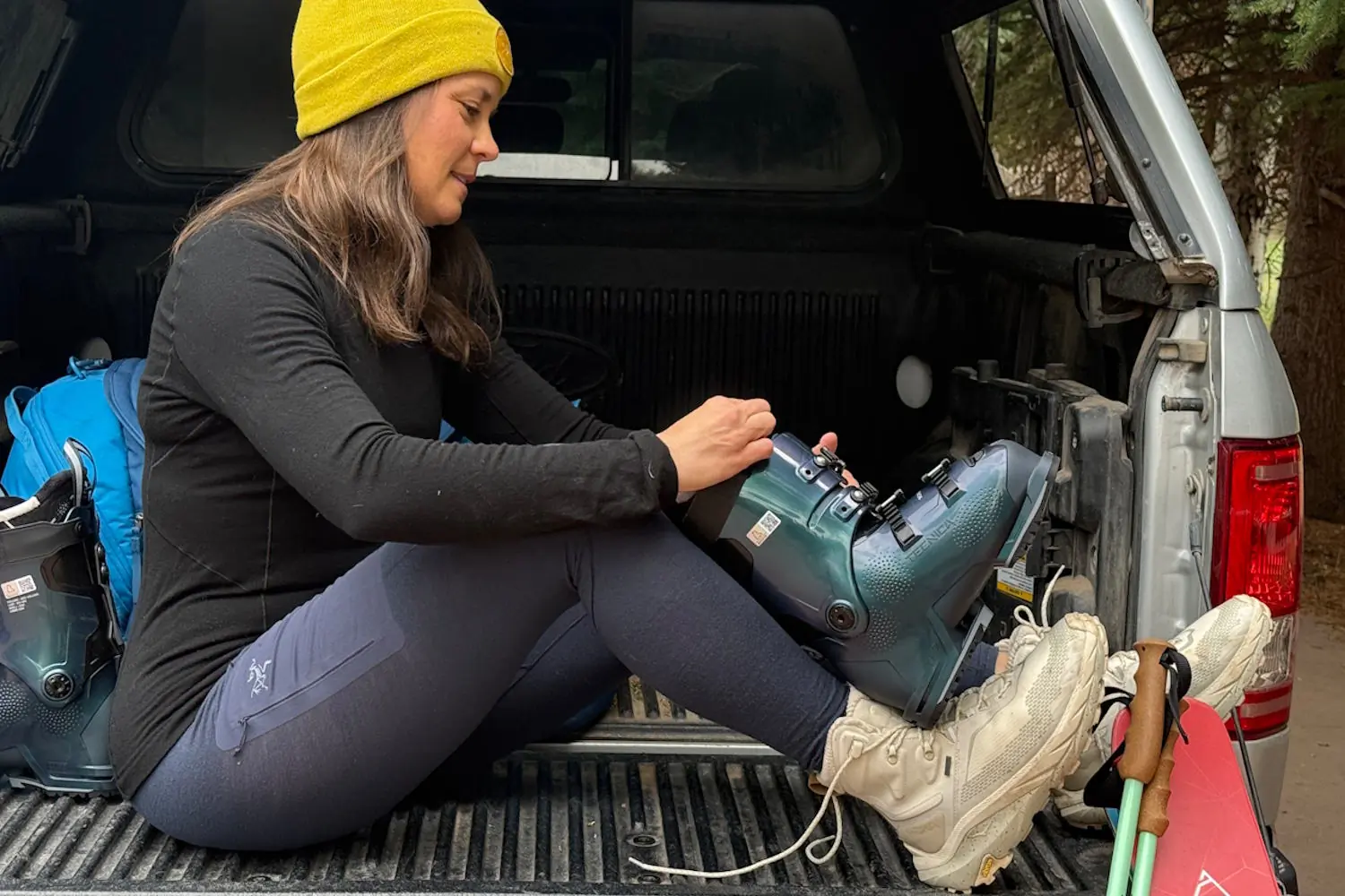 A woman wearing an Arc'teryx Satoro crew neck shirt, matching leggings, and a yellow beanie sits on the tailgate of a truck