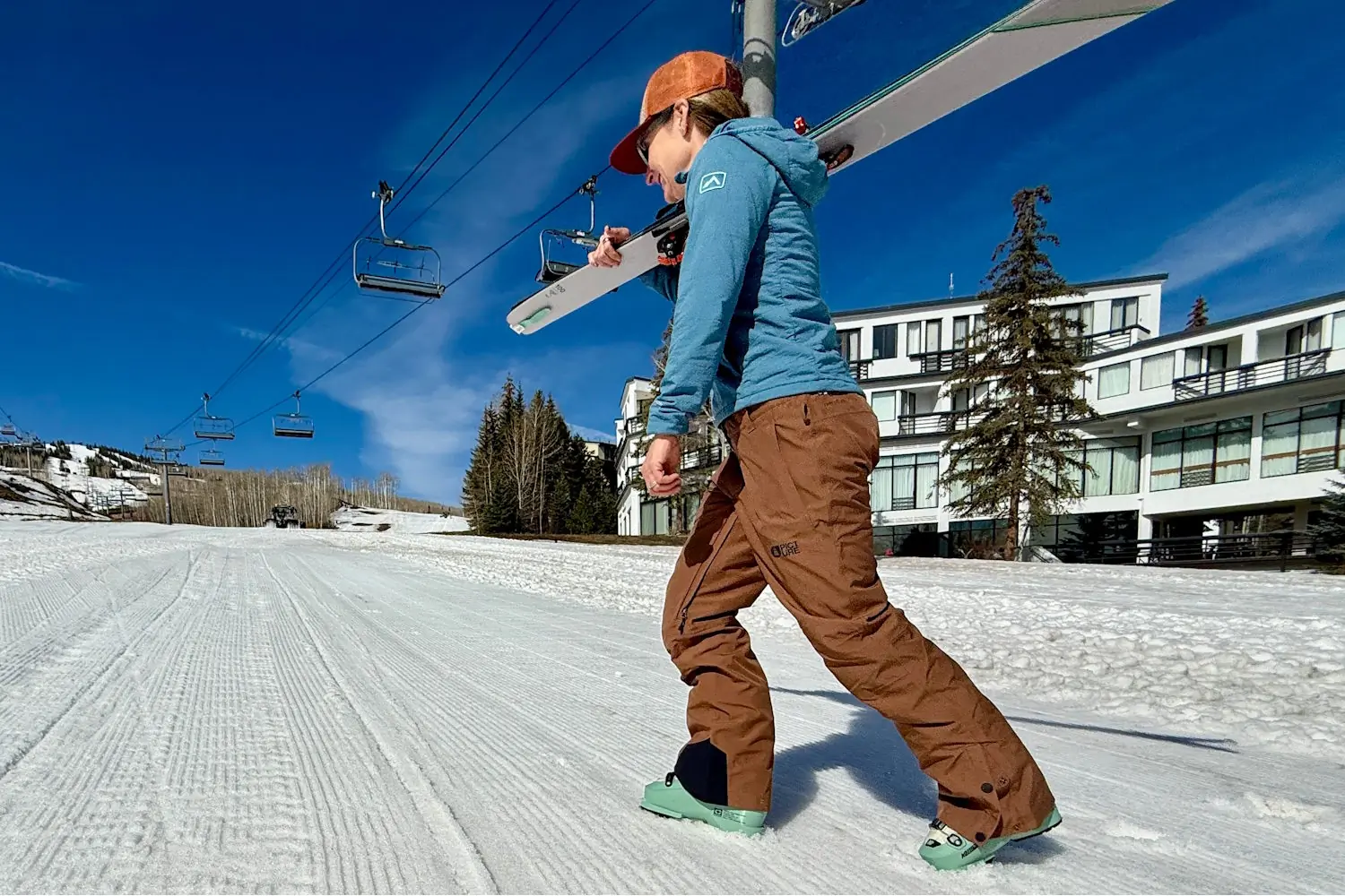A person wearing Exa snow pants walks on a snowy slope carrying ski
