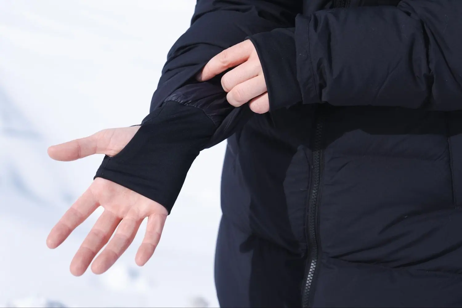 A woman wearing the OR Coze Down Parka with her hand showing wrist gaiters with thumbholes at the end of the sleeve.